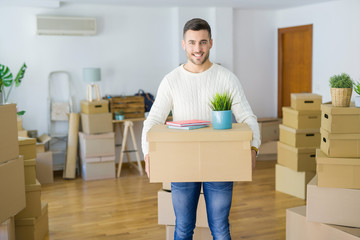 Handsome man holding cardboard box at new apartment, smiling very happy moving to a new house