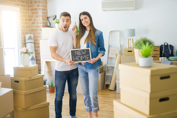 Fototapeta na wymiar Young beautiful couple holding blackboard with new home text at new house surprised with an idea or question pointing finger with happy face, number one