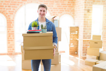 Handsome young man smiling happy moving to a new home, very excited holding cardboard boxes at new apartment