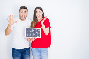 Young beautiful couple holding blackboard with new home text over white isolated background very happy and excited, winner expression celebrating victory screaming with big smile and raised hands