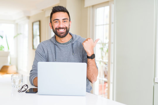 Handsome hispanic man working using computer laptop pointing and showing with thumb up to the side with happy face smiling