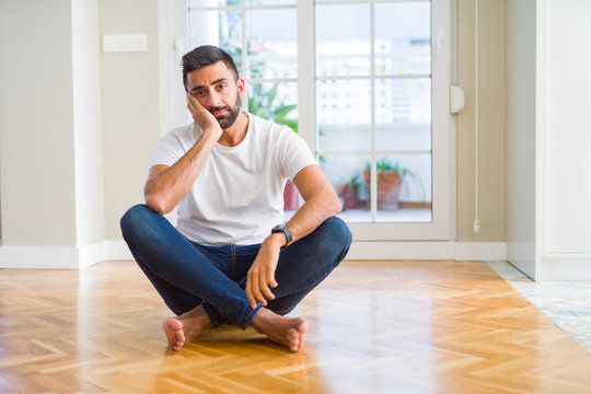 Handsome hispanic man wearing casual t-shirt sitting on the floor at home thinking looking tired and bored with depression problems with crossed arms.