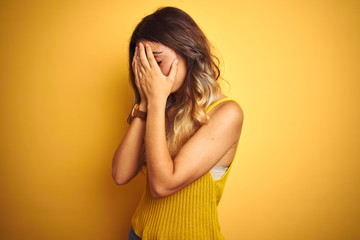 Young beautiful woman wearing t-shirt over yellow isolated background with sad expression covering face with hands while crying. Depression concept.