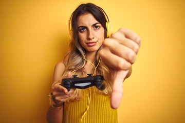 Young beautiful woman playing video game using gamepad over yellow isolated background with angry...