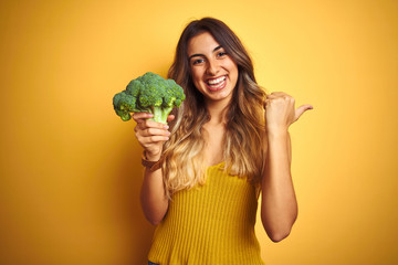 Young beautiful woman eating broccoli over yellow isolated background pointing and showing with...