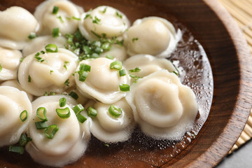 Bowl of tasty dumplings in broth on table, closeup