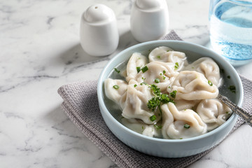 Bowl of tasty dumplings in broth with spoon on white marble table. Space for text