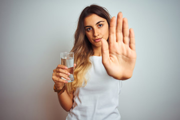 Young beautiful woman drinking a glass of water over white isolated background with open hand doing stop sign with serious and confident expression, defense gesture
