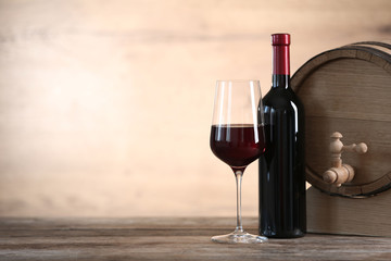 Fototapeta na wymiar Glass and bottle of red wine near wooden barrel on table. Space for text