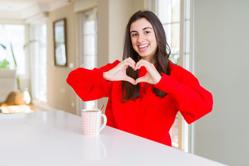 Beautiful young woman drinking a cup of black coffee smiling in love showing heart symbol and shape with hands. Romantic concept. - Powered by Adobe