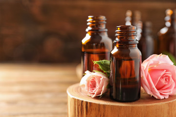 Bottles of rose essential oil and fresh flowers on table, closeup. Space for text