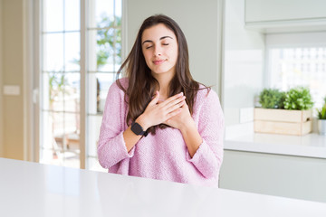 Beautiful young woman wearing pink sweater smiling with hands on chest with closed eyes and grateful gesture on face. Health concept.