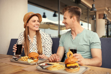 Young happy couple with burgers in street cafe