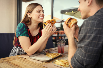 Young couple eating burgers in street cafe