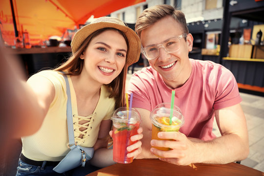 Young couple with summer drinks taking selfie in street cafe
