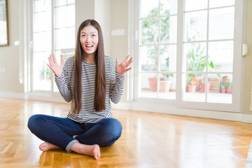 Beautiful Asian woman sitting barefoot on the floor at home crazy and mad shouting and yelling with...