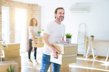 Middle age senior couple moving to a new house, man smiling happy in love with new apartment and holding cardboard boxes