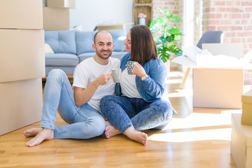 Fototapeta na wymiar Young couple sitting on the floor of new house arround cardboard boxing, relaxing from moving drinking a cup of coffee smiling very happy