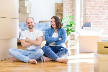 Young couple sitting on the floor arround cardboard boxes moving to a new house happy face smiling with crossed arms looking at the camera. Positive person.