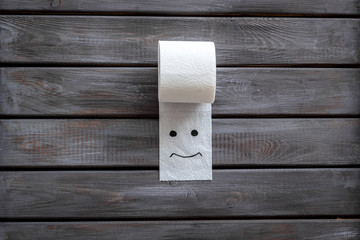 Toilet paper roll with painted face for proctology diseases concept on wooden background top view