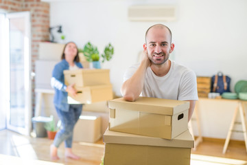 Young couple moving to new apartment, handsome man leaning on cardboard boxes and smiling happy