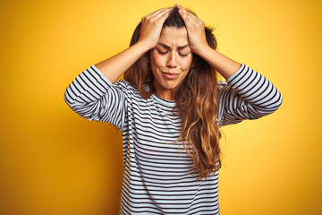 Young beautiful woman wearing stripes t-shirt standing over yelllow isolated background suffering from headache desperate and stressed because pain and migraine. Hands on head.