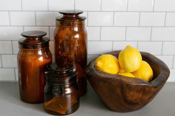 Lemons in Wooden Bowl and Amber Jars on Concrete Kitchen Countertop, White Subway Tile Backsplash