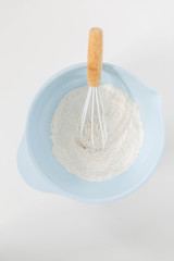 Light Blue Mixing Bowl With Flour, White Background, White and Wood Whisk