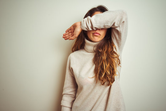 Young beautiful woman wearing winter sweater standing over white isolated background covering eyes with arm, looking serious and sad. Sightless, hiding and rejection concept
