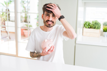 Young man holding piggy bank as insurance investment stressed with hand on head, shocked with shame and surprise face, angry and frustrated. Fear and upset for mistake.