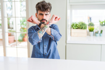 Young man wearing casual shirt sitting on white table Rejection expression crossing arms doing negative sign, angry face