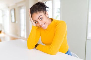 Beautiful young african american woman smiling cheerful leaning on the table comfortable