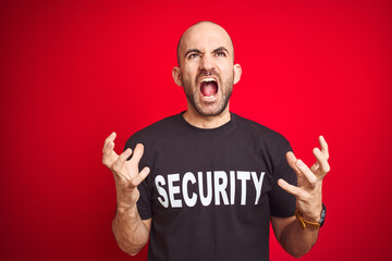 Young safeguard man wearing security uniform over red isolated background crazy and mad shouting...
