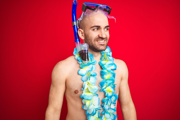 Young man wearing diving snorkel goggles and hawaiian lei flowers over isolated red background...
