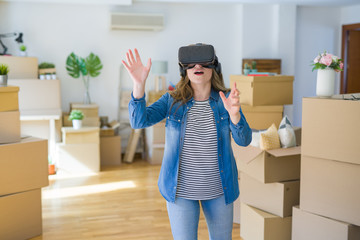 Obraz na płótnie Canvas Young blonde woman wearing virtual reality glasses playing a simulation game around cardboard boxes moving to a new house