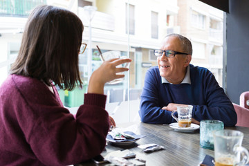 Senior man having a conversation with woman drinking coffee and relaxing, chatting at restaurant