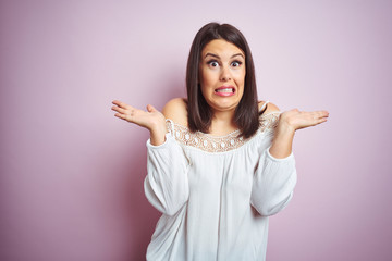 Young beautiful brunette woman over pink isolated background clueless and confused expression with...
