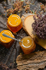 A table with a wicker table top, honey in honeycombs on a wooden board, honey in an open glass jar, with medicinal herbs oregano, chamomile and strawberry flowers. flower pollen collected by bees