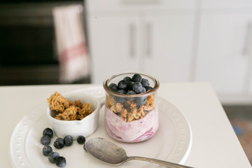 Blueberry Yogurt in Clear Glass with Fresh Blueberries and Honey Granola, Modern Kitchen Background