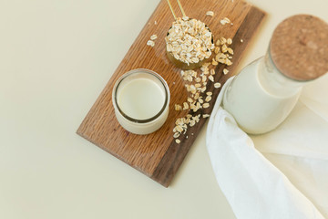 Fresh Oat Milk in a Clear Glass with Bottle, Loose Oats, Off-White Background, Homemade, Top View
