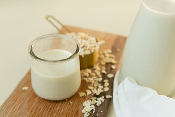 Fresh Oat Milk in a Clear Glass with Bottle, Loose Oats, Off-White Background, Homemade, Top View