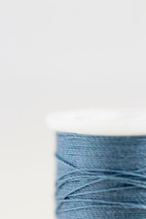 Spool of blue thread with very limited focus on white background. Extreme close-up/