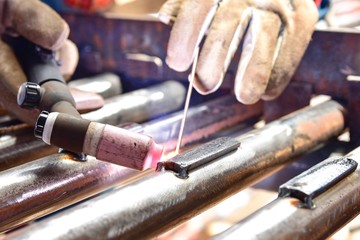 The welder is welding the plate to the pipe with Tungsten Inert Gas Welding process (TIG). The welder wears protective equipment with a mask and heat resistant gloves