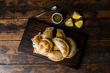 Traditional baked Argentine empanadas savoury pastries with meat beef stuffing against wooden background