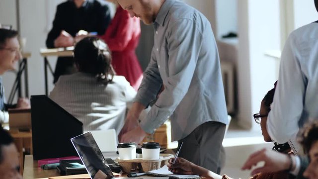 Happy young Caucasian businessman working at busy healthy workplace. Diverse people work, communicate at modern office.