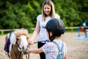 Cute little girl and her older sister enjoying with pony horse outdoors at ranch.