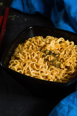 Ramen noodles bowl on a dark textured background with dark wooden chopsticks