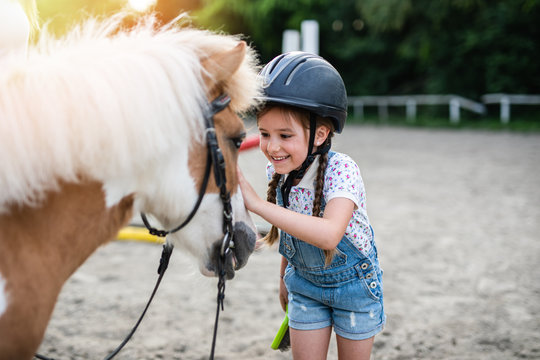 Cute little girl enjoying with pony horse outdoors at ranch.