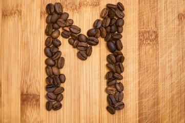 Alphabet letter M made from roasted coffee beans, 3D rendering on wooden table background