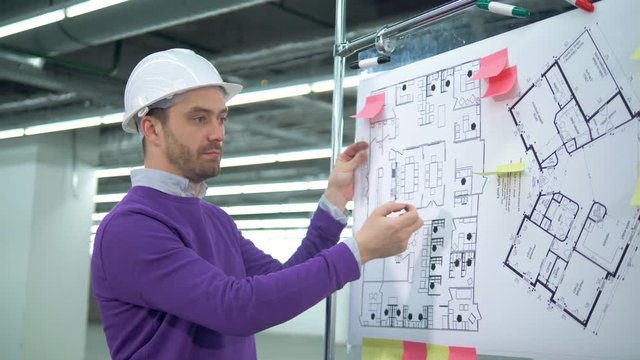 An architect in a hardhat is inspecting layouts